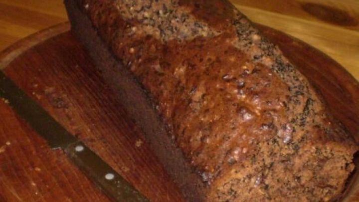 Schokoladenkuchen liegt auf rundem Holzbrett, daneben ein Messer; rustikaler Tischhintergrund.