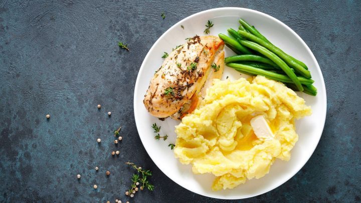 Zarte Schnibbelbohnen und cremige Kartoffeln liegen auf einem wei&szlig;en Teller, umgeben von frischen Kr&auml;utern und Pfefferk&ouml;rnern.