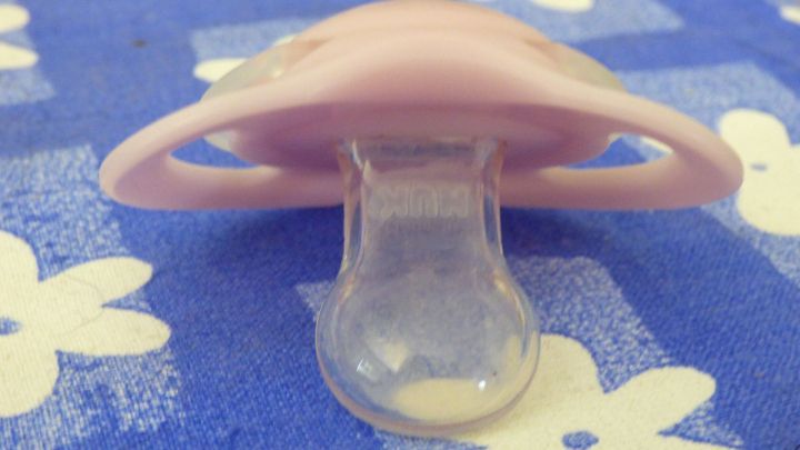 Ein rosa Schnuller liegt auf einem blauen Stoff mit wei&szlig;en Blumen, bereit, einem Baby beim Abgew&ouml;hnen zu helfen.