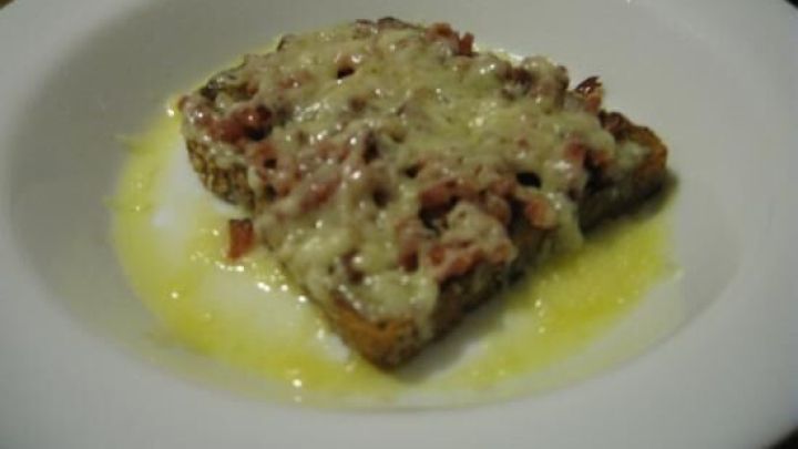 Ein &uuml;berbackenes Toastbrot liegt auf einem wei&szlig;en Teller, umgeben von geschmolzenem K&auml;se und leichtem &Ouml;l.