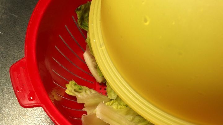 Ein gelber Salatspinner ist auf einem roten Sieb platziert, w&auml;hrend frisch gewaschener Salat darin wartet, geschleudert zu werden.