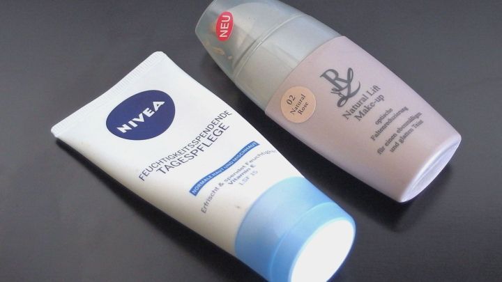 Eine Nivea-Gesichtscreme und ein Make-up-Produkt liegen auf einem schwarzen Untergrund, bereit, aufgetragen zu werden.