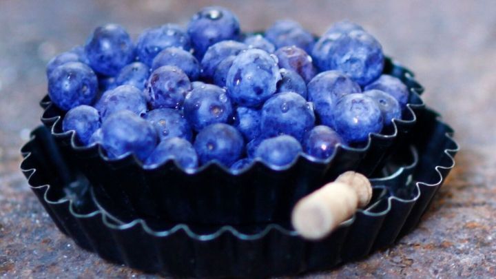 Eine schwarze Backform enth&auml;lt frische, leuchtend blaue Blaubeeren, die auf einem rustikalen Tisch pr&auml;sentiert werden.