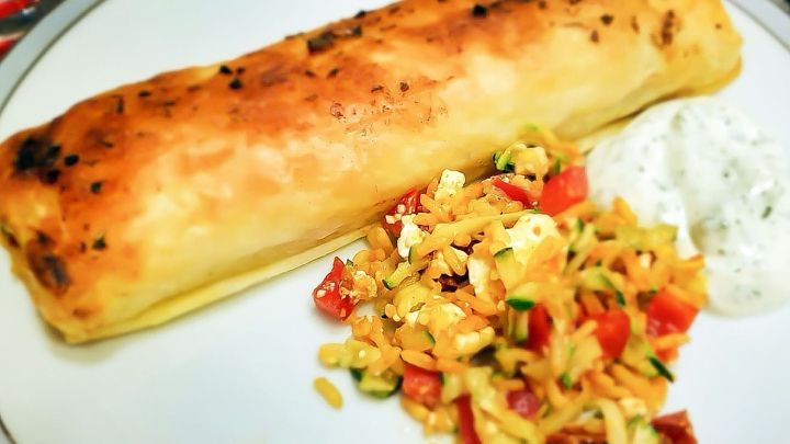 Ein knuspriger Strudel, gef&uuml;llt mit Kartoffeln und Spinat, liegt auf dem Teller neben frischem Salat und Joghurt-Dip.