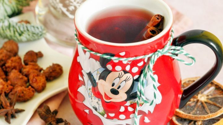 Ein roter Kinderpunsch in einer Minni-Maus-Tasse dampft neben Gew&uuml;rzen und Trockenfr&uuml;chten auf einem Tisch.
