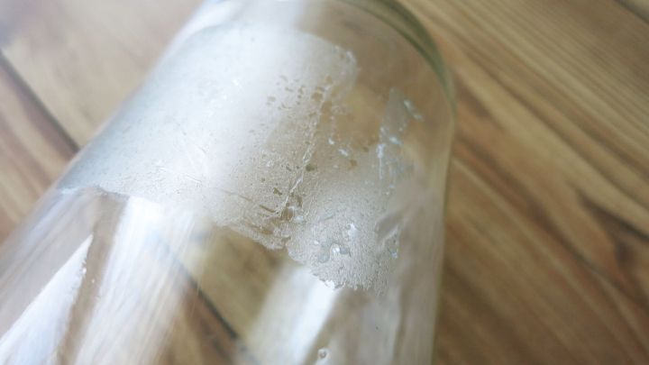 Ein Glas ist auf einer Holzoberfl&auml;che zu sehen, beschlagen mit Reinigungsmitteln, die zur Entfernung von Kleberesten verwendet werden.
