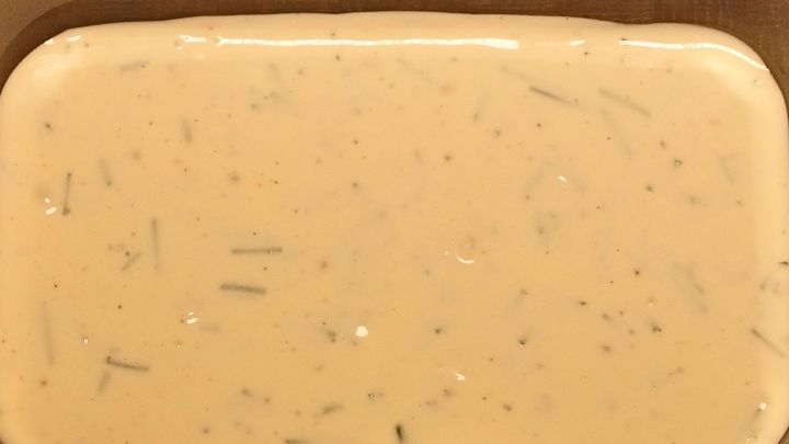 Ein cremiger Kr&auml;uterquark liegt in einer flachen Sch&uuml;ssel auf einem Holztisch, bereit zum Servieren oder Genie&szlig;en.