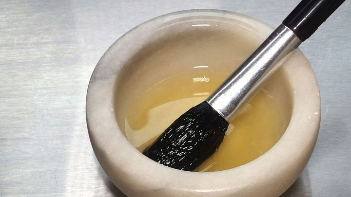 Ein M&ouml;rser enth&auml;lt Eiwei&szlig;, w&auml;hrend ein Pinsel darin eingetaucht ist, um die Anwendung f&uuml;r ein Peeling vorzubereiten.