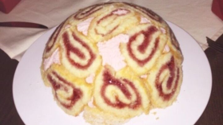 Eine runde Biskuit-Torte auf einem Teller zeigt eine Anordnung von Spiral-Rollen mit Himbeerf&uuml;llung, appetitlich dekoriert.