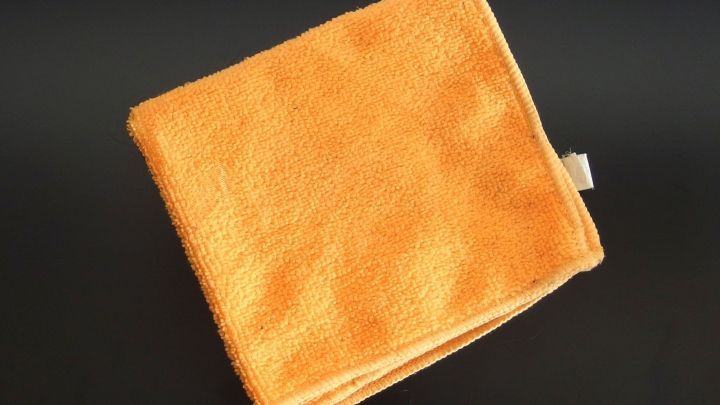 Ein orangefarbener Putzlappen liegt gefaltet auf einem dunkelgrauen Hintergrund, bereit zum Reinigen in einem Haushalt.