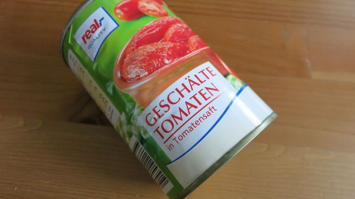 Ein Konservenglas mit gesch&auml;lten Tomaten liegt schr&auml;g auf einem Holzuntergrund, bereit zur Verwendung in Gerichten.