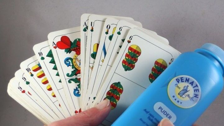 Eine Hand h&auml;lt zusammenklebende Spielkarten, w&auml;hrend daneben ein blauer Flaschenbeh&auml;lter mit Pflegeprodukt steht.