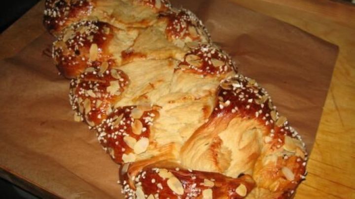 Ein gebackener Hefezopf liegt frisch auf einem Holzbrett, bestreut mit Zucker und Mandeln, im K&uuml;chenumfeld.