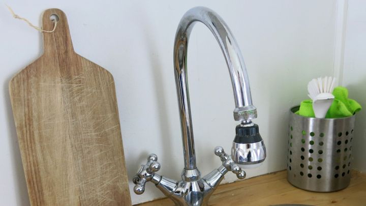 Ein gl&auml;nzender Wasserhahn wird in einer K&uuml;che gereinigt, um stumpfe Armaturen mit Gallseife aufzuhellen. Ein Holzbrett liegt daneben.