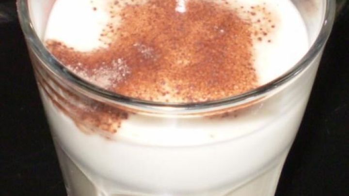 Ein Glas Kaffee mit Sojamilch und einem Hauch Zimt steht auf einem Tisch, umgeben von einer eleganten Atmosph&auml;re.