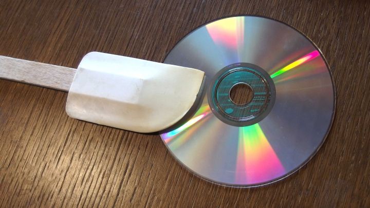 Ein Holzspatel liegt auf einer CD, die auf einer Holzoberfl&auml;che platziert ist, und wird als Teigschaber verwendet.