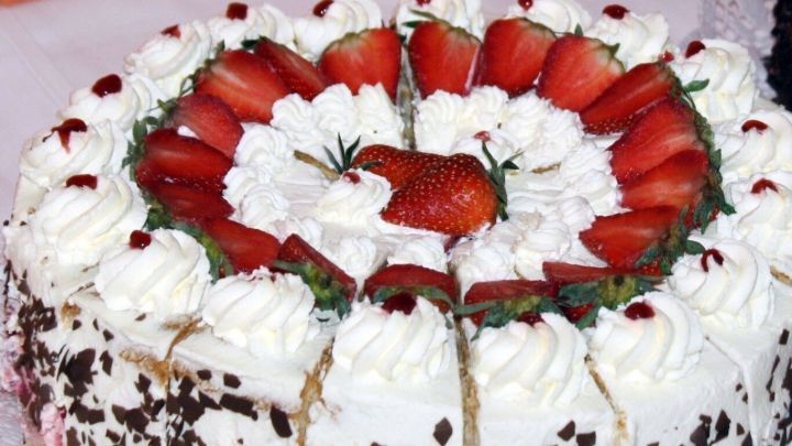 Eine Erdbeertorte, &uuml;ppig dekoriert mit Sahne und frischen Erdbeeren, steht auf einem Tisch, bereit zum Servieren.