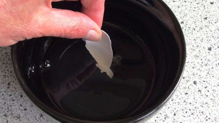 Eine Hand hebt eine Eierschale aus einem schwarzen Beh&auml;lter, w&auml;hrend sie &uuml;ber einer glatten Oberfl&auml;che schwebt.