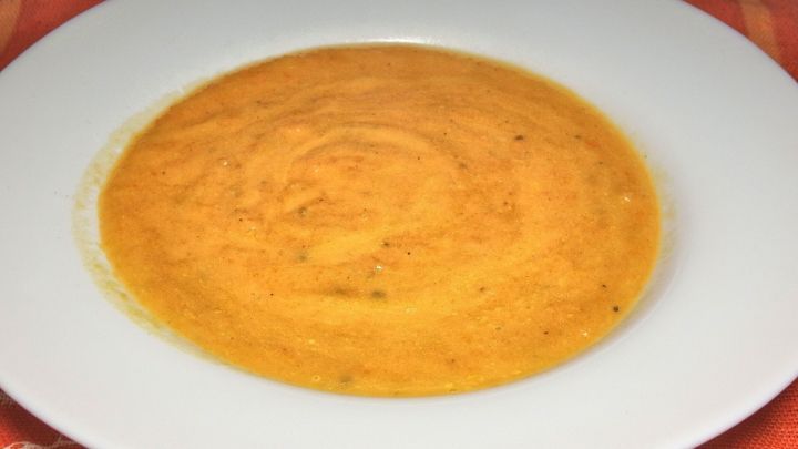 Eine cremige M&ouml;hrencremesuppe in einer wei&szlig;en Sch&uuml;ssel, serviert auf einem farbigen Tisch.