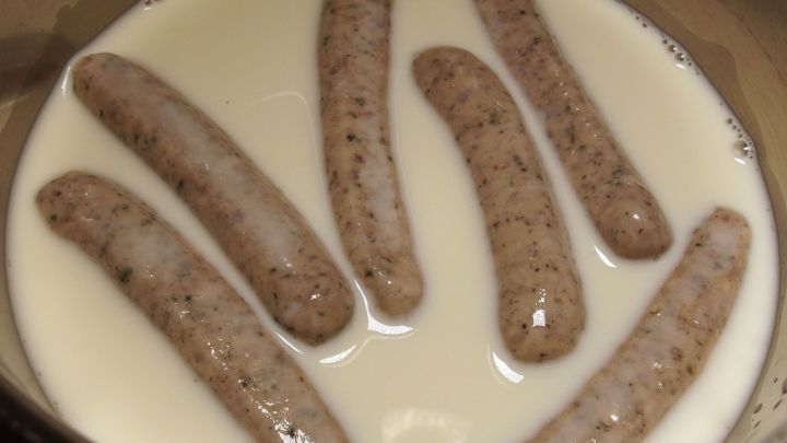 Bratw&uuml;rste liegen in einem Topf mit Milch, um das Aufplatzen beim Kochen zu verhindern.