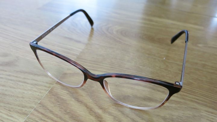 Eine Brille liegt auf einem Holztisch und ist dabei, mit einem Glaskeramikreiniger gereinigt zu werden.