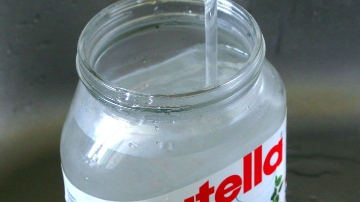 Ein Beh&auml;lter mit hei&szlig;em Wasser wird &uuml;ber einem Nutella-Glas gegossen, um Aufkleber zu entfernen.