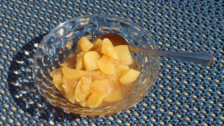 Ein glasierter Teller mit eingekochtem Obst steht im Sonnenlicht, bereit zum Servieren, auf einem blauen Tuch.