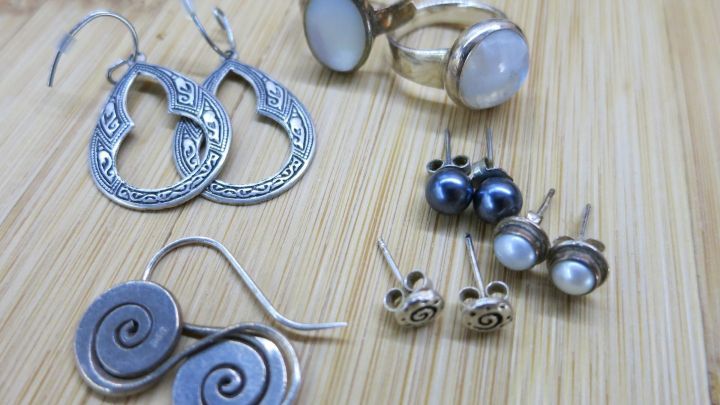 Silberschmuck liegt auf einem Holztisch, w&auml;hrend Oxi Waschkraftverst&auml;rker zur Reinigung bereitsteht.