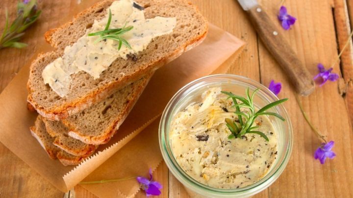 Kr&auml;uterbutter liegt auf ger&ouml;stetem Brot, w&auml;hrend ein Glas mit zus&auml;tzlicher, kalorienarmer Kr&auml;uterbutter im Vordergrund steht.