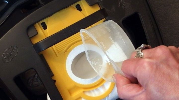 Ein Hand greift nach einem Messbecher, um Fl&uuml;ssigkeit in einen Staubsaugerbeh&auml;lter zu gie&szlig;en, um schlechte Luft zu vermeiden.