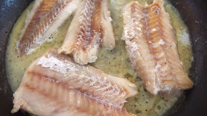 Frittierter Fisch liegt in einer Pfanne in hei&szlig;em Fett und verstr&ouml;mt einen intensiven Fischgeruch in der K&uuml;che.