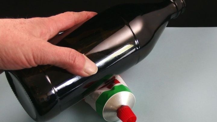 Eine Hand h&auml;lt eine gro&szlig;e schwarze Flasche, w&auml;hrend sie &uuml;ber eine Tube mit rotem Verschluss gleitet, um sie restlos zu leeren.