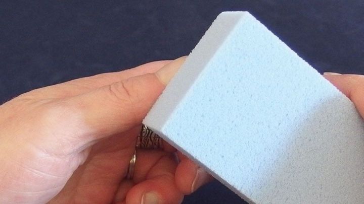 Ein Bimsstein wird von einer Hand gehalten, um superkleber von fingern zu entfernen, auf einem neutralen Hintergrund.