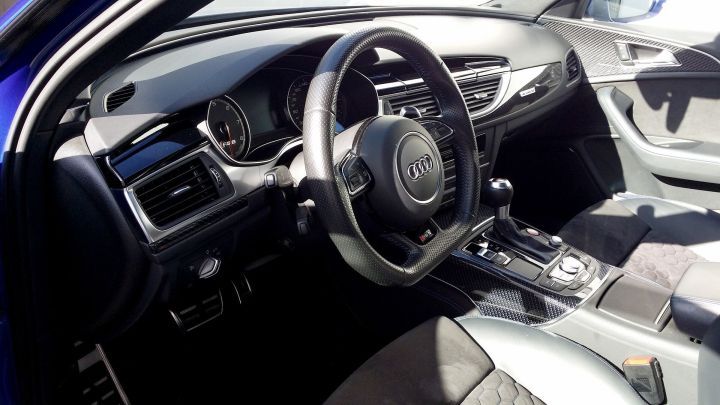 Lenkrad mit Audi-Logo steht im Vordergrund, eingebaut in schwarzes Armaturenbrett eines modernen Autos bei hellem Tageslicht.