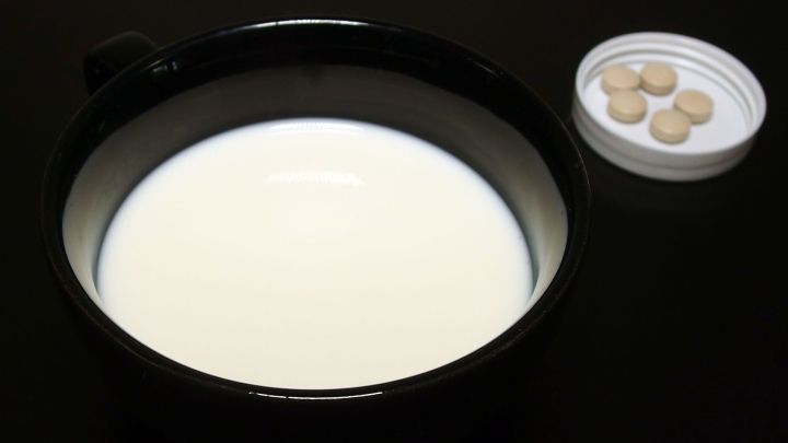 Eine schwarze Sch&uuml;ssel mit frischer Milch steht auf einem Tisch, daneben eine Dose mit Hautpflege-Tabletten.