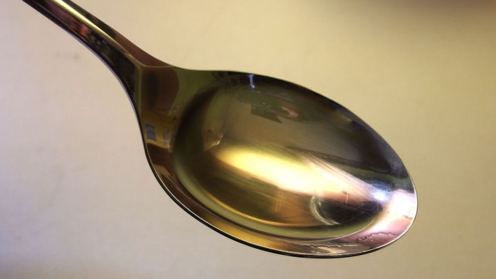 Eine Edelstahl-L&ouml;ffel schimmert in der Beleuchtung, bereit f&uuml;r die Anwendung einer &Ouml;lziehkur zur Infektpr&auml;vention.
