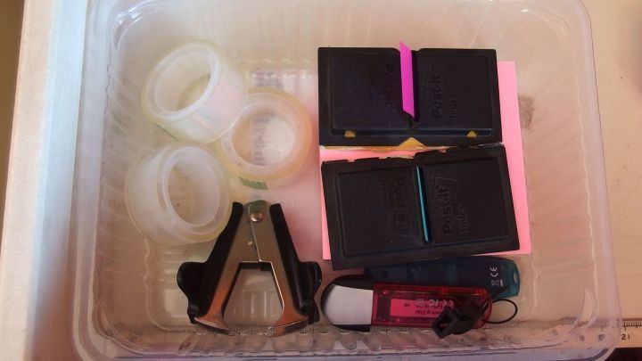 In einer durchsichtigen Box befinden sich Fleischverpackungen, Heftklammern und Notizen, die Ordnung im Schreibtisch schaffen.