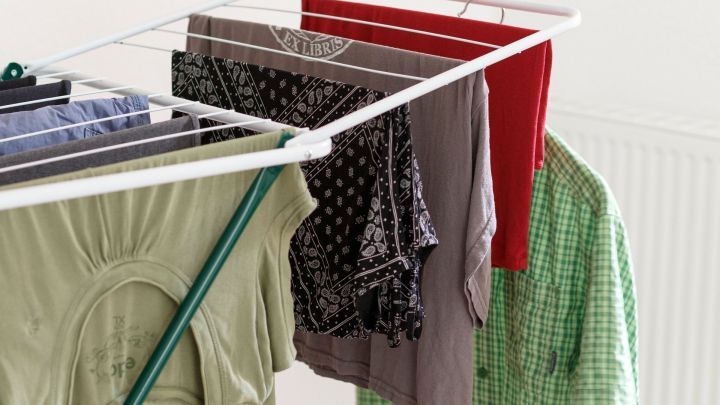 Bunte W&auml;sche h&auml;ngt auf einem W&auml;schest&auml;nder, frisch gewaschen, in einem hellen Raum mit neutraler Wandfarbe.