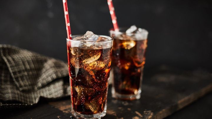 Zwei Gl&auml;ser Sekt Cola mit Eisw&uuml;rfeln stehen auf einem rustikalen Holzbrett, umgeben von einer dunklen, gem&uuml;tlichen Umgebung.