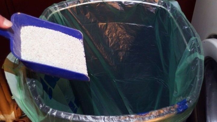 Eine Schaufel mit Katzenstreu wird in einen M&uuml;llbeutel in einem M&uuml;lleimer geleert, um Ger&uuml;che zu reduzieren.