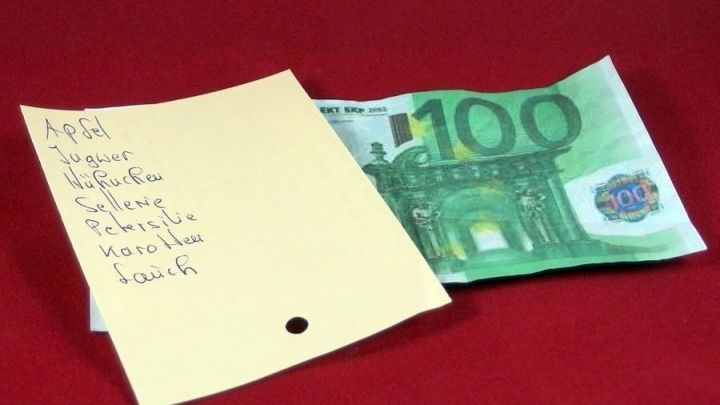 Ein gelbes Einkaufsnotizblatt liegt neben einem 100-Euro-Schein auf rotem Hintergrund, was zum Thema Einkauftipps anregt.