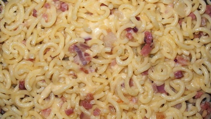 Eine cremige K&auml;seso&szlig;e umh&uuml;llt spiralige Nudeln mit w&uuml;rzigen Speckst&uuml;ckchen in einer Pfanne.