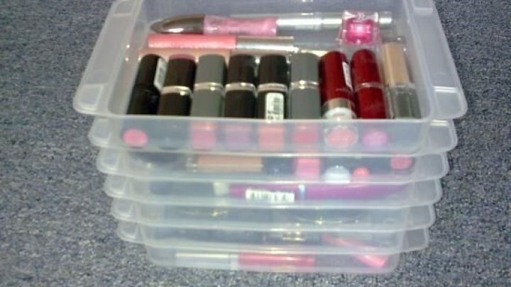 Transparente Box mit ordentlich angeordneten Schminkartikeln, darunter Lippenstifte in verschiedenen Farben, auf einer Fl&auml;che.