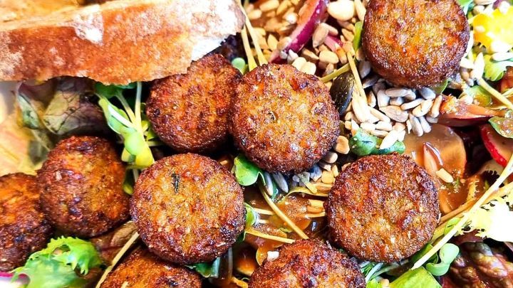 Kleine, frittierte vegetarische Bulettchen liegen auf einem bunten Salat mit Brotst&uuml;cken im Hintergrund.