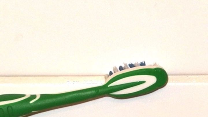 Eine gr&uuml;ne Zahnb&uuml;rste steht auf einer wei&szlig;en Oberfl&auml;che und wartet darauf, f&uuml;r die Reinigung von verdreckten Fugen verwendet zu werden.