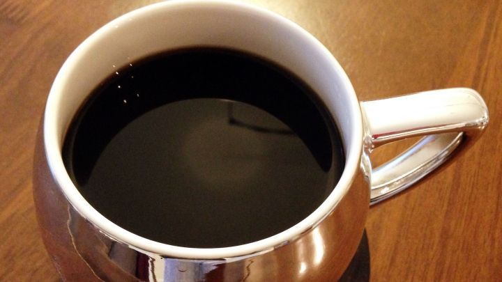 Eine elegante Tasse Kaffee steht auf einem Holzuntersetzer. Der schwarze Kaffee strahlt ein tolles Aroma aus.