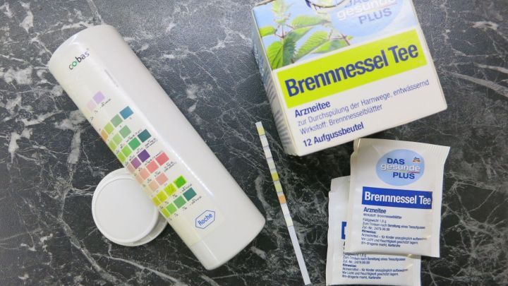 Teepackungen und ein Teststreifen auf schwarzem Marmortisch, Brennnessel Tee von DAS gesunde PLUS mit Anweisungen.