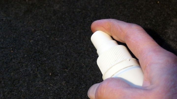 Eine Hand hält eine Sprühflasche, die auf einen schmutzigen Auto-Innenraum zeigt, um die ausgelaufene Milch zu reinigen.
