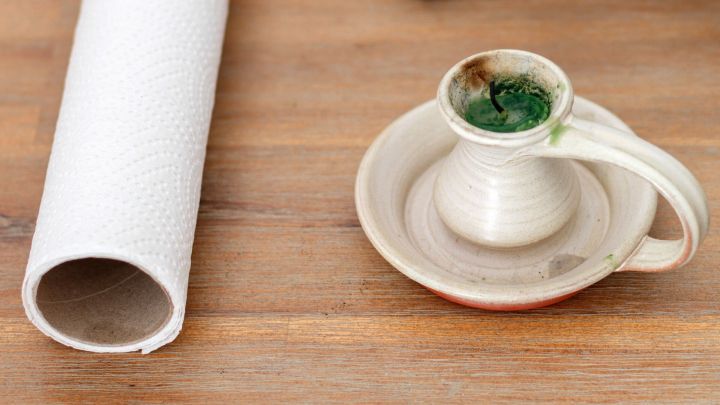 Kerzenst&auml;nder mit gr&uuml;nen Kerzenresten auf einem Holzuntergrund. Daneben liegt eine leere K&uuml;chenpapierrolle.