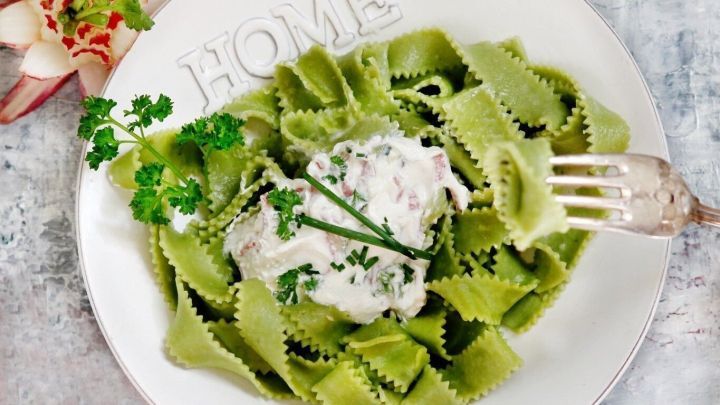 Gr&uuml;ne Bandnudeln liegen auf einem Teller, dar&uuml;ber ist eine cremige Schinken-Sahne-Sauce mit frischen Kr&auml;utern.